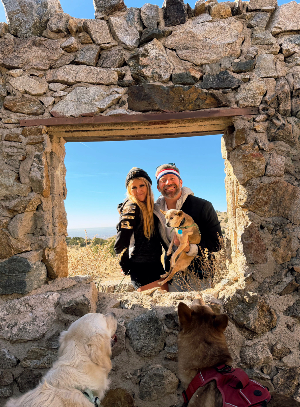 Two people and one dog smiling with two dogs enjoying through stone window on hike