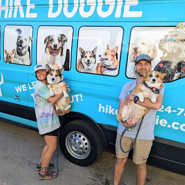Two staff members posing beside branded dog hiking van