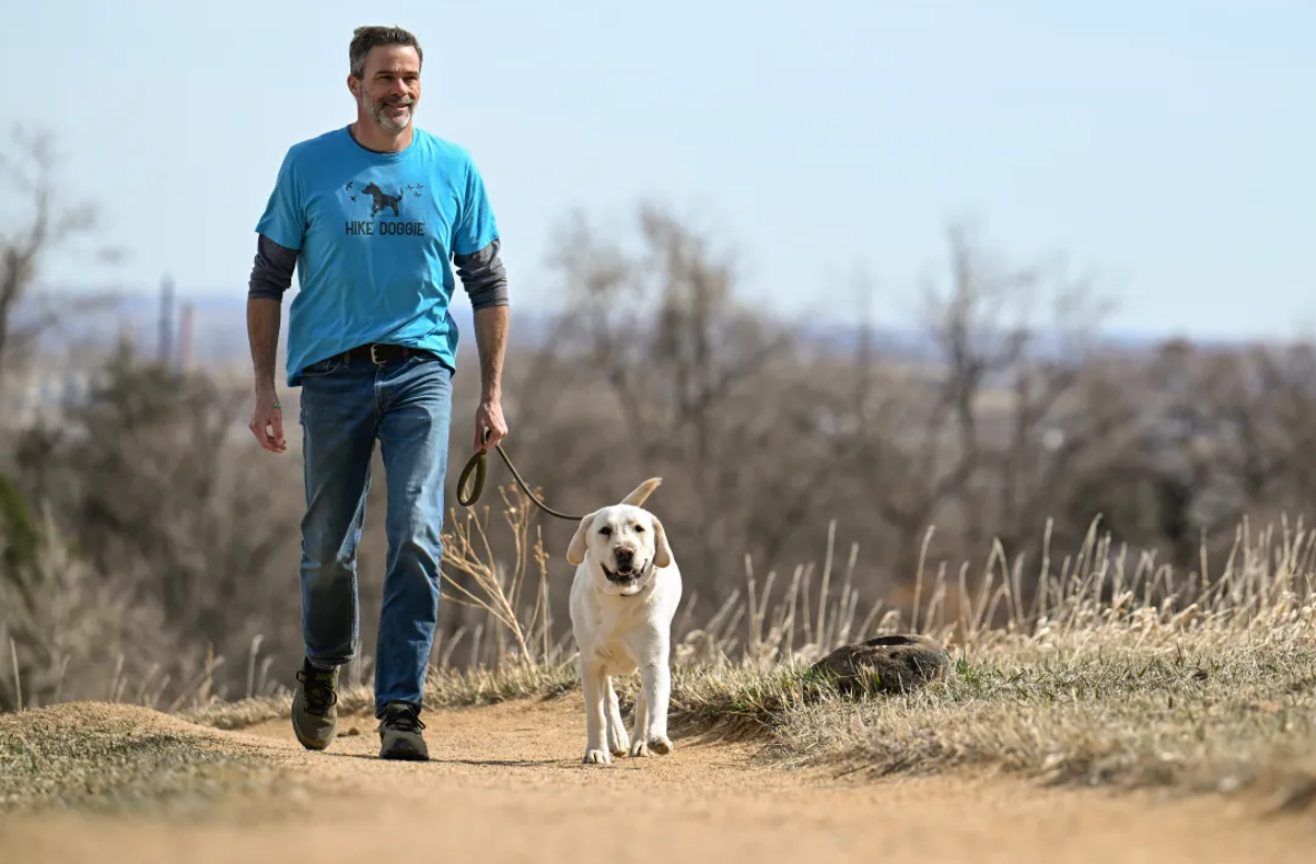 Man walking with white dog on dirt trail
