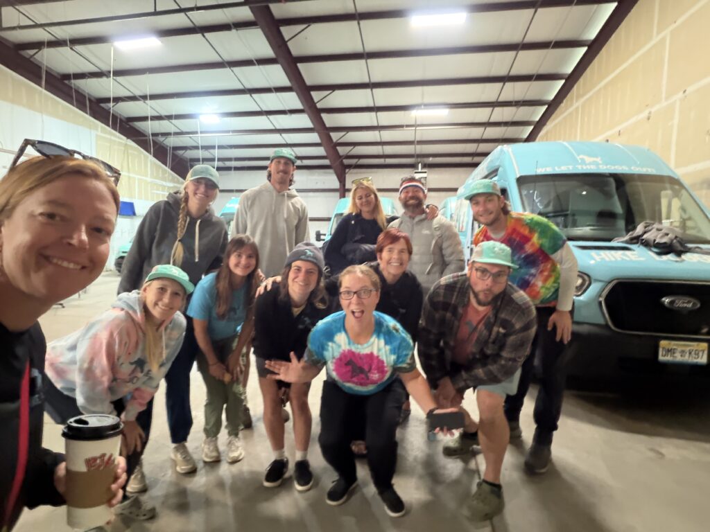 Hike Doggie team photo — staff and handlers gathered in front of a Hike Doggie van, celebrating 10 years of dog hiking adventures